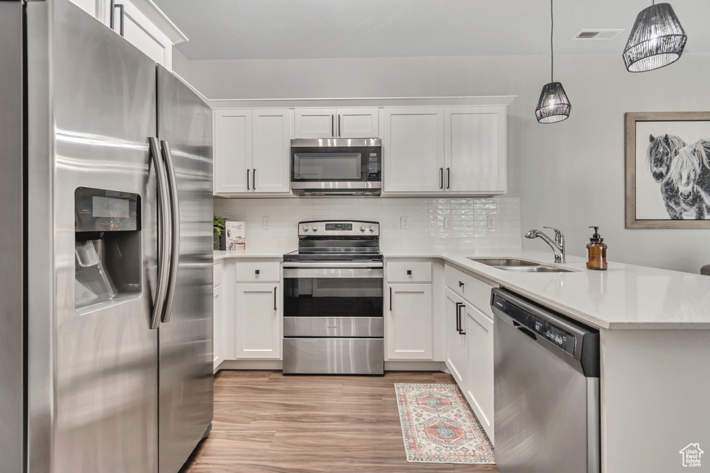 Kitchen featuring appliances with stainless steel finishes, a peninsula, light wood-type flooring, light countertops, and decorative backsplash