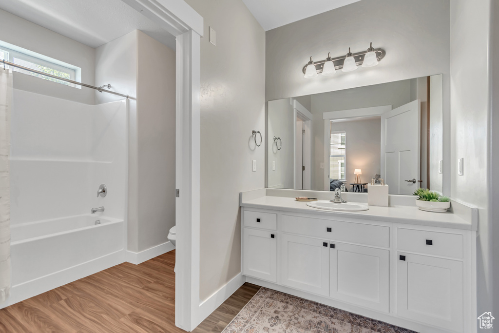Bathroom featuring toilet, bathtub / shower combination, vanity, wood finished floors, and baseboards