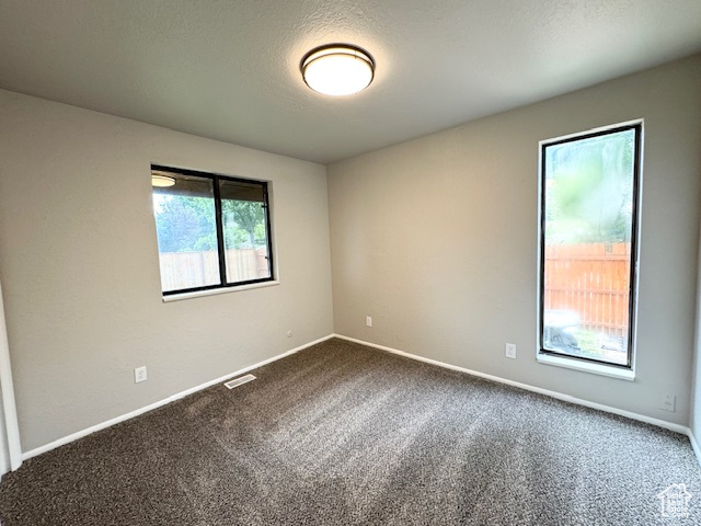 Spare room featuring dark carpet and baseboards