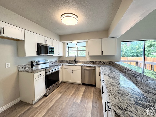 Kitchen with stainless steel appliances, a sink, light wood-style floors, a textured ceiling, and light stone countertops