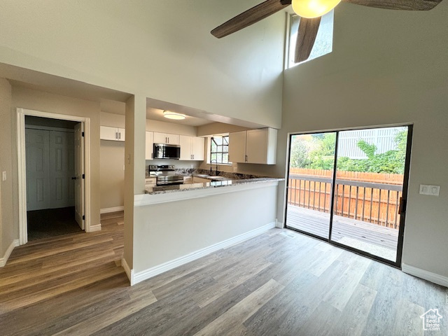 Kitchen featuring stainless steel appliances, a ceiling fan, white cabinetry, light wood-style flooring, and a towering ceiling