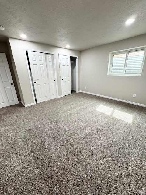 Unfurnished bedroom featuring a textured ceiling, multiple closets, baseboards, recessed lighting, and carpet flooring