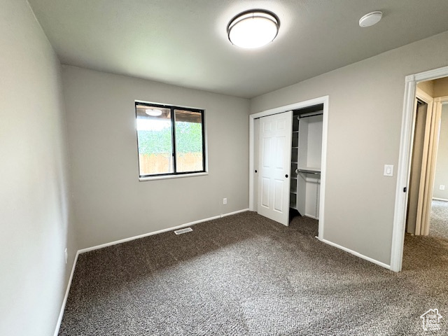 Unfurnished bedroom featuring dark colored carpet, baseboards, and a closet