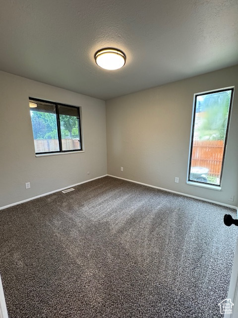 Unfurnished room featuring dark carpet, baseboards, and a textured ceiling