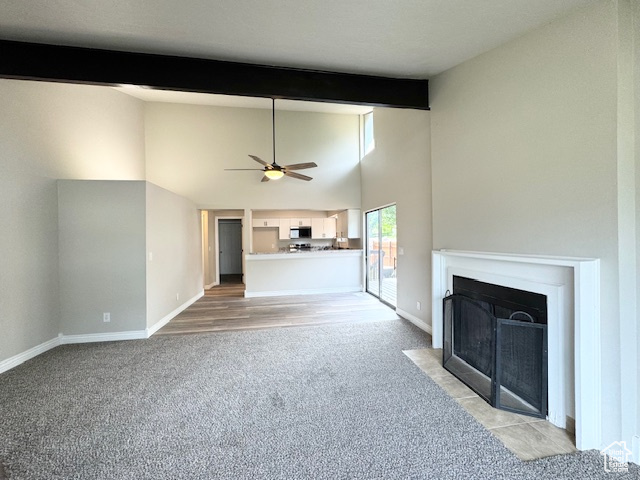 Unfurnished living room with light carpet, beam ceiling, a ceiling fan, a fireplace with flush hearth, and baseboards