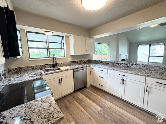 Kitchen featuring dishwasher, a sink, light wood-style flooring, white cabinetry, and a textured ceiling