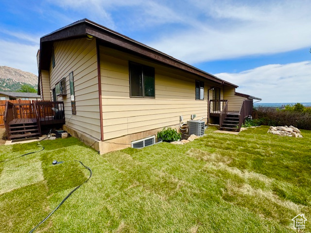 View of side of property featuring a wooden deck, central AC unit, and a yard