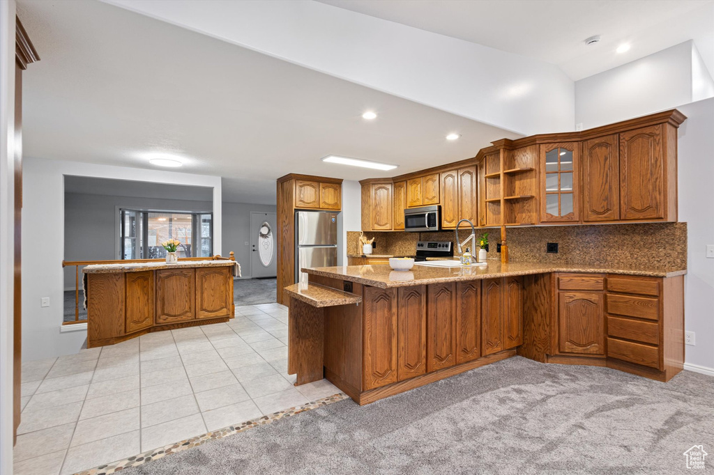 Kitchen with stainless steel appliances, a peninsula, brown cabinetry, a sink, and light stone counters
