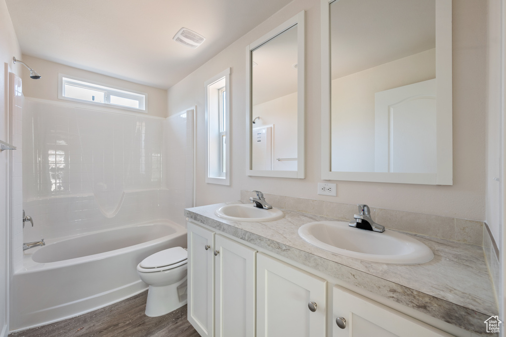 Bathroom featuring toilet, double vanity, shower / bathtub combination, and wood finished floors