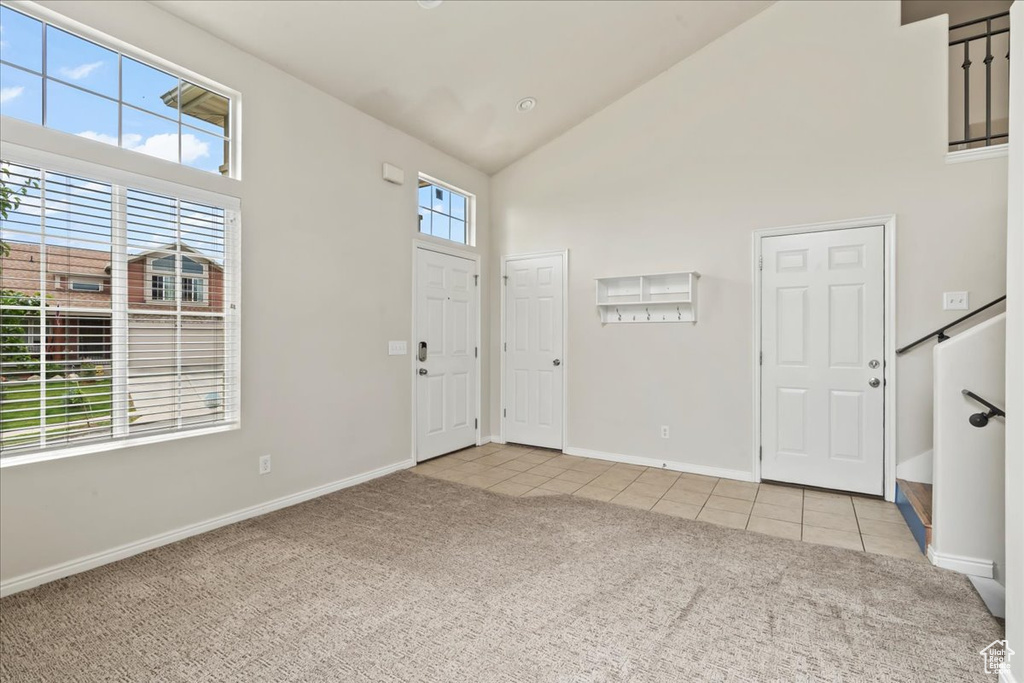 Foyer with light colored carpet, high vaulted ceiling, light tile patterned floors, and baseboards