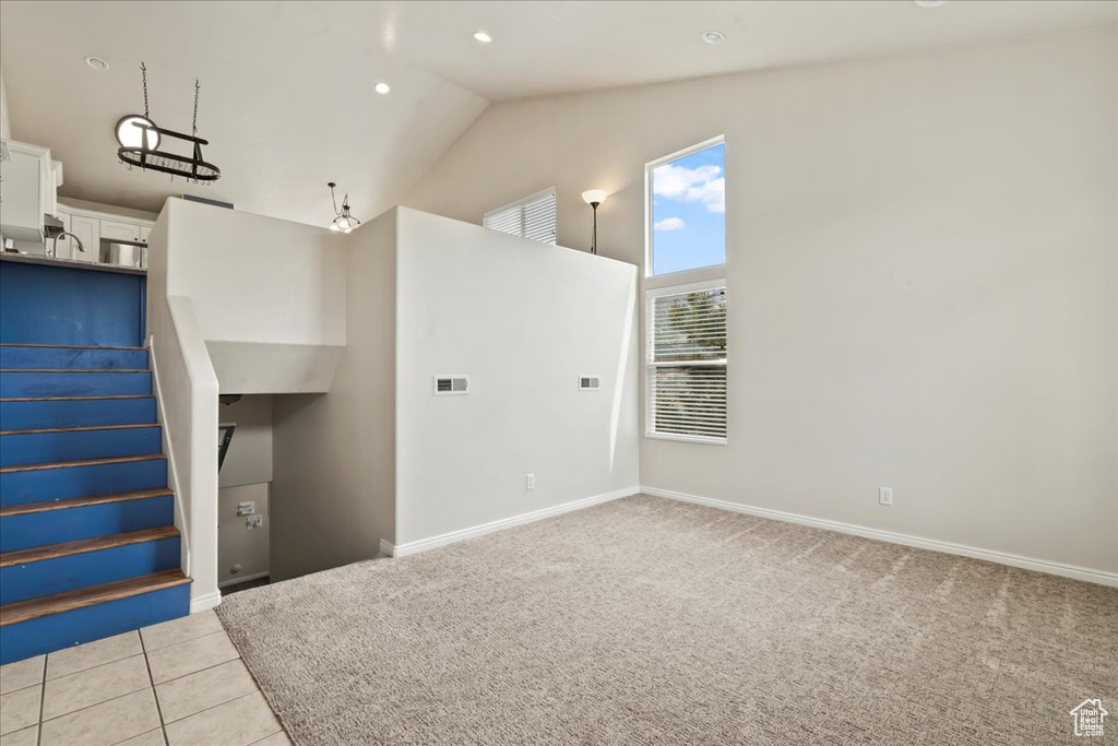 Empty room featuring stairs, light carpet, baseboards, high vaulted ceiling, and light tile patterned flooring