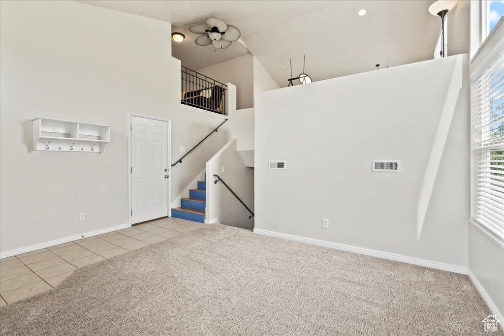 Carpeted empty room with tile patterned floors, a high ceiling, baseboards, and stairway