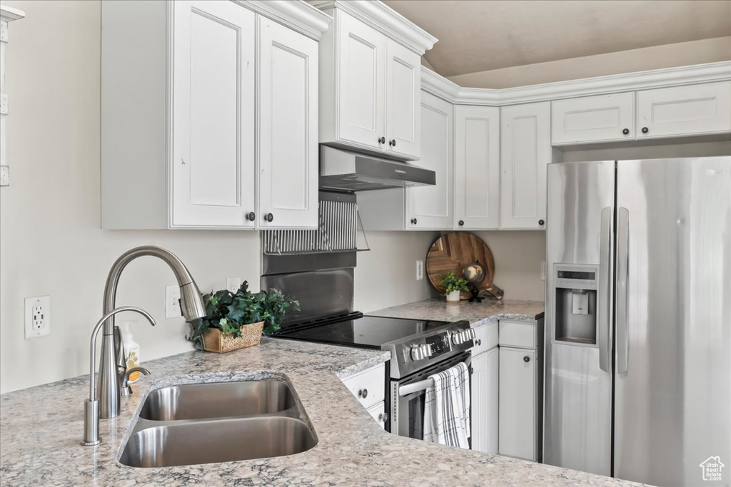 Kitchen with appliances with stainless steel finishes, under cabinet range hood, a sink, and white cabinetry