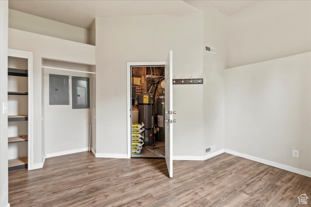 Unfurnished bedroom featuring electric panel, wood finished floors, a closet, baseboards, and a towering ceiling