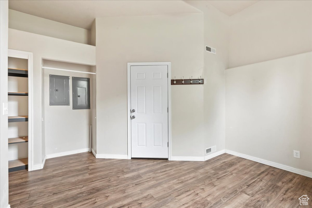 Unfurnished room featuring electric panel, wood finished floors, baseboards, and a high ceiling