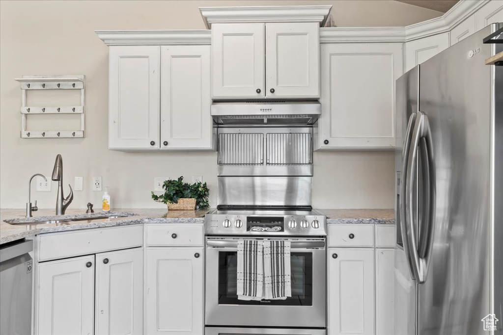 Kitchen featuring stainless steel appliances, under cabinet range hood, a sink, white cabinetry, and light stone countertops