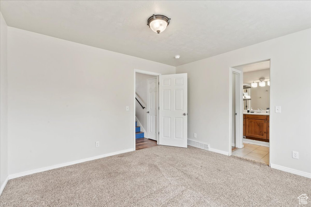 Unfurnished bedroom with light colored carpet, baseboards, connected bathroom, and a sink