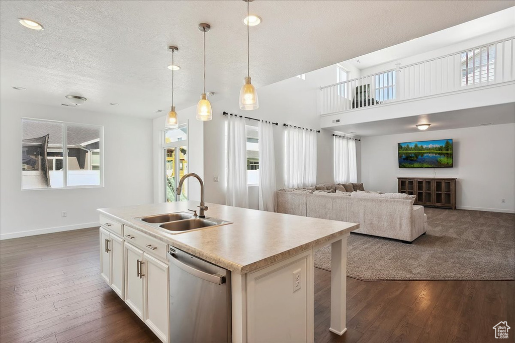 Kitchen featuring stainless steel dishwasher, a sink, baseboards, dark wood-style floors, and an island with sink