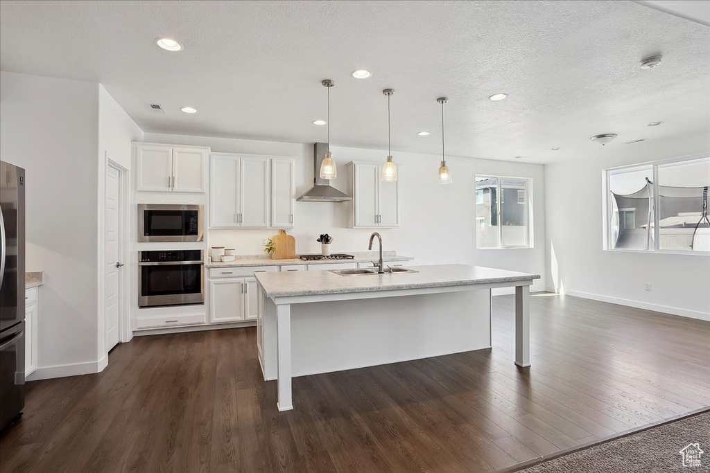 Kitchen featuring appliances with stainless steel finishes, wall chimney exhaust hood, a sink, baseboards, and dark wood-type flooring
