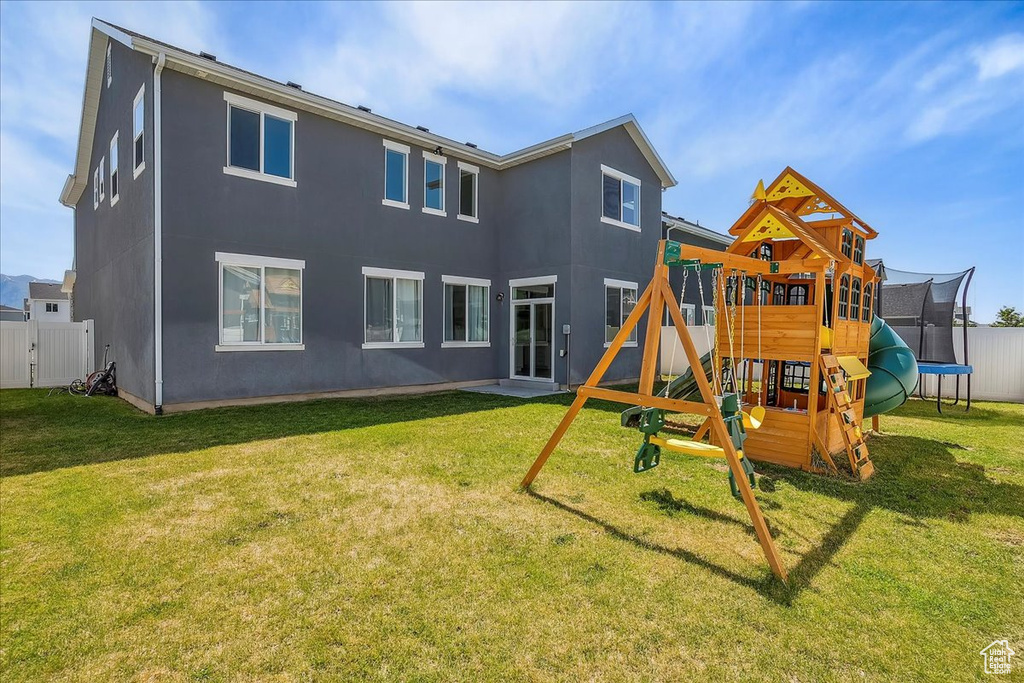 Back of property with a trampoline, a playground, and stucco siding