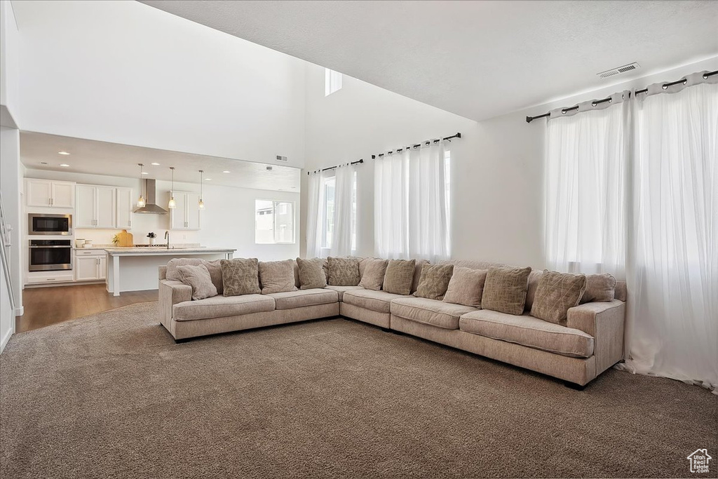Living area featuring plenty of natural light, light wood-style floors, a towering ceiling, light carpet, and recessed lighting