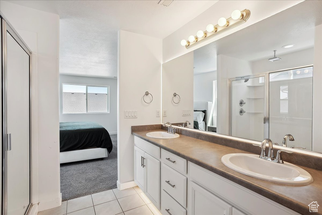 Ensuite bathroom featuring a shower stall, tile patterned flooring, double vanity, and baseboards
