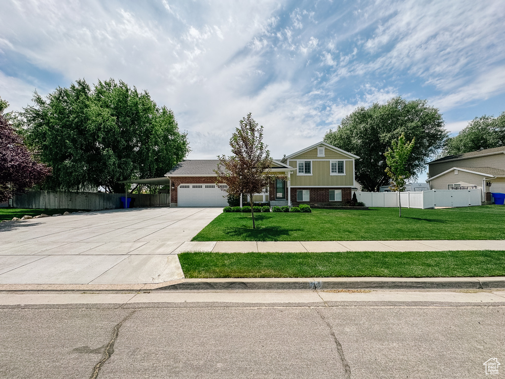 Split level home featuring brick siding, driveway, an attached garage, and an attached carport