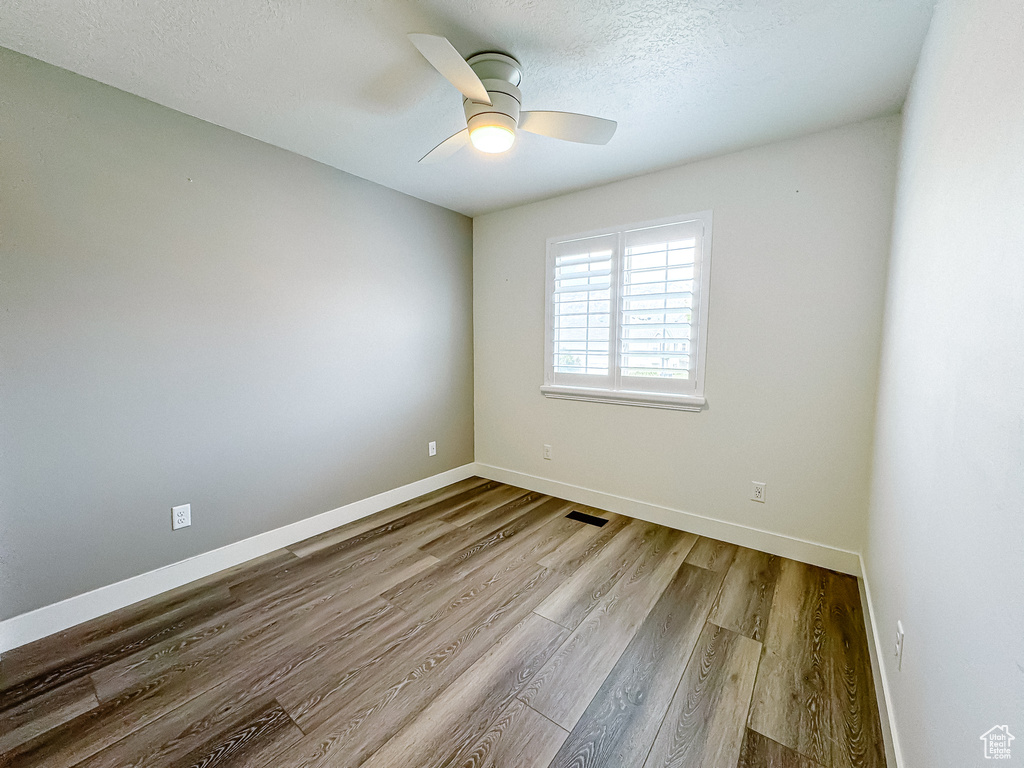 Empty room featuring wood finished floors, a ceiling fan, baseboards, and a textured ceiling