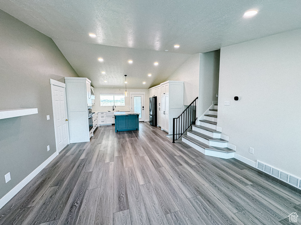 Unfurnished living room featuring lofted ceiling, wood finished floors, stairs, a sink, and baseboards