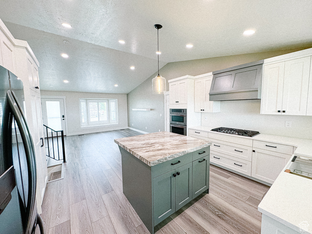 Kitchen featuring freestanding refrigerator, gas cooktop, stainless steel double oven, custom range hood, and light countertops