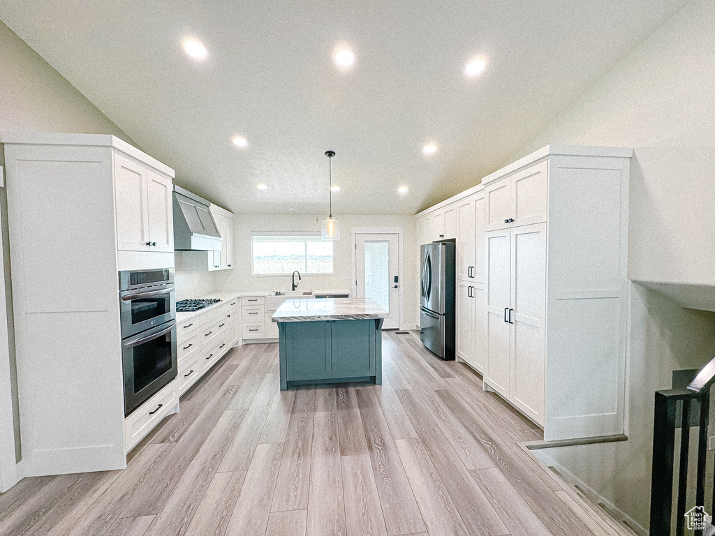 Kitchen with appliances with stainless steel finishes, recessed lighting, wall chimney range hood, light wood-style floors, and white cabinetry