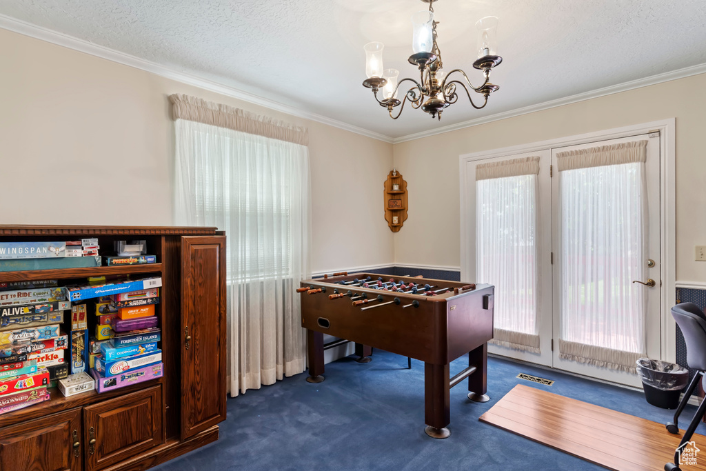Rec room featuring a chandelier, plenty of natural light, dark colored carpet, and ornamental molding