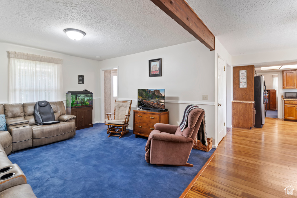 Living area with a textured ceiling, light wood-type flooring, and beam ceiling
