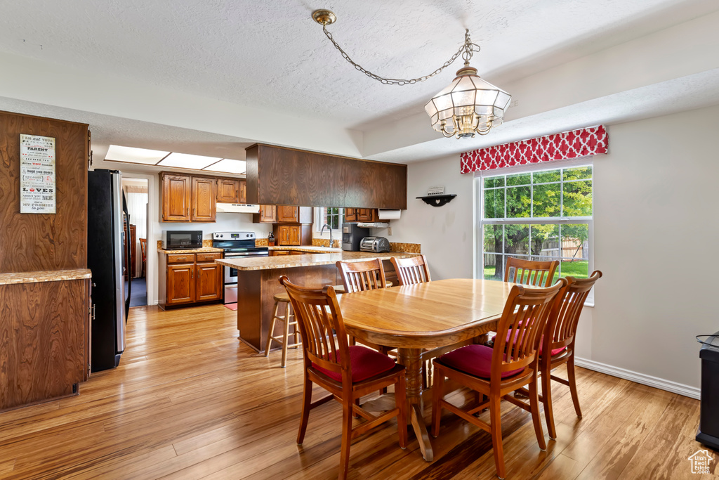 Dining space with light wood-type flooring, a textured ceiling, a chandelier, and baseboards