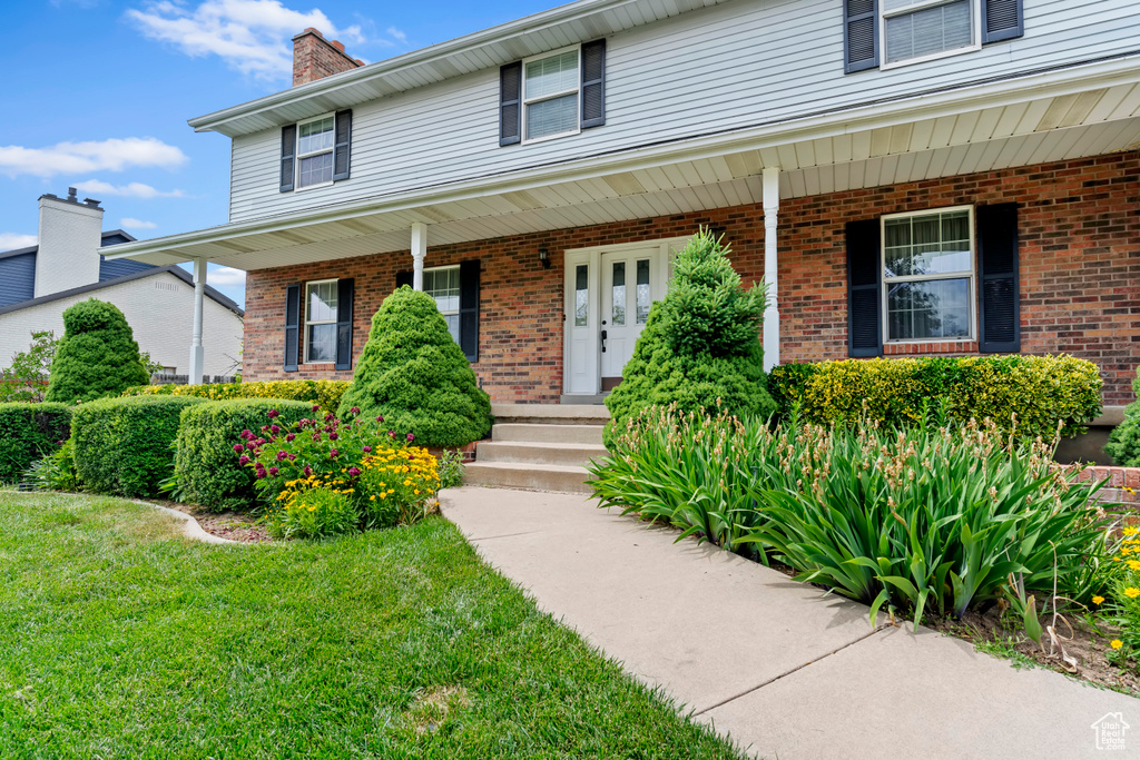View of front of home with covered porch, brick siding, a chimney, and a front yard