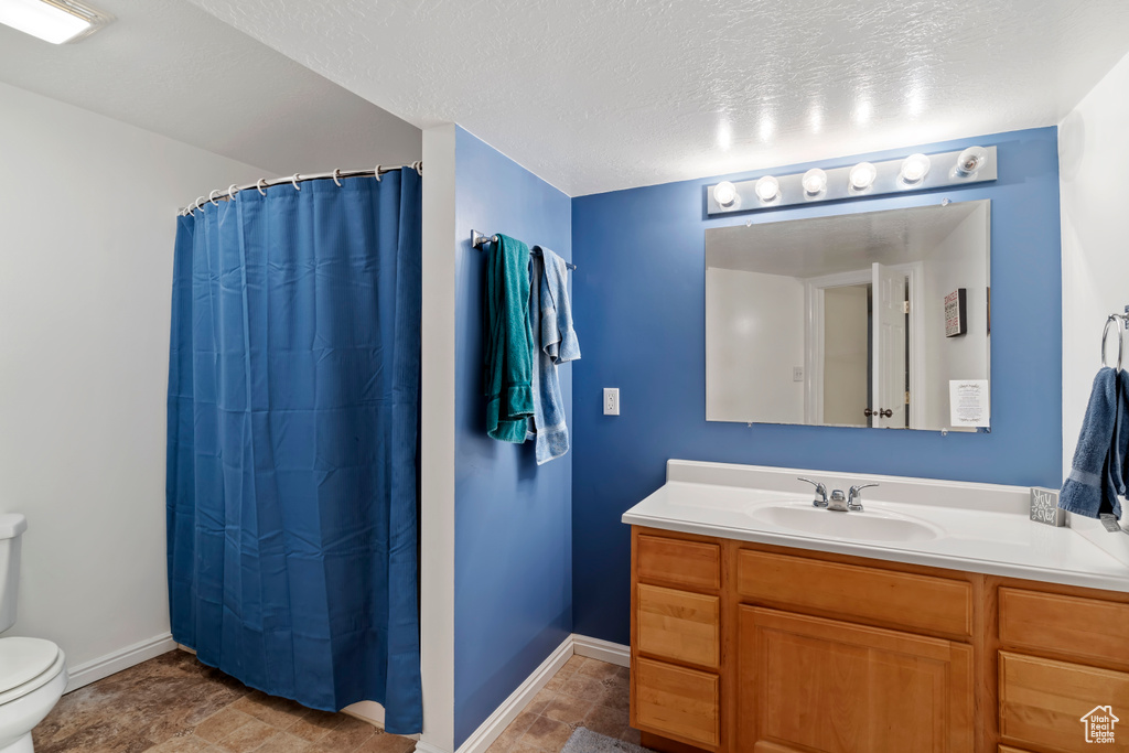 Full bath featuring toilet, stone finish floors, baseboards, vanity, and a textured ceiling