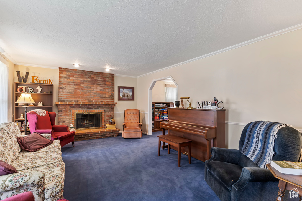 Living room featuring crown molding, dark carpet, a textured ceiling, a brick fireplace, and arched walkways