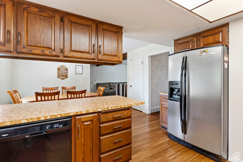 Kitchen featuring stainless steel fridge, black dishwasher, light wood-style flooring, and light countertops