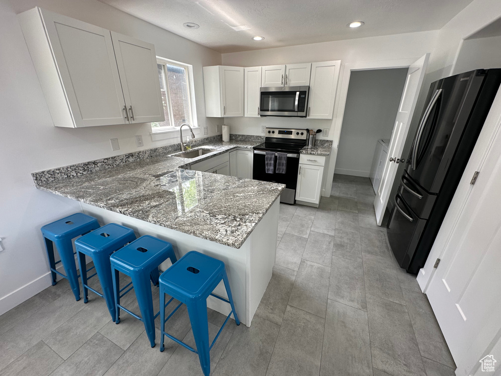 Kitchen featuring stainless steel appliances, a sink, light stone counters, a peninsula, and a kitchen breakfast bar