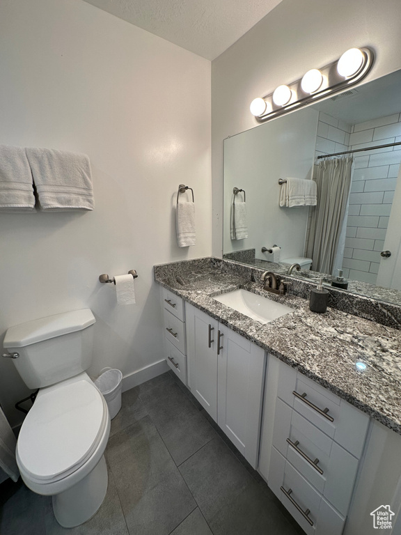 Full bath featuring toilet, vanity, baseboards, tiled shower, and tile patterned flooring