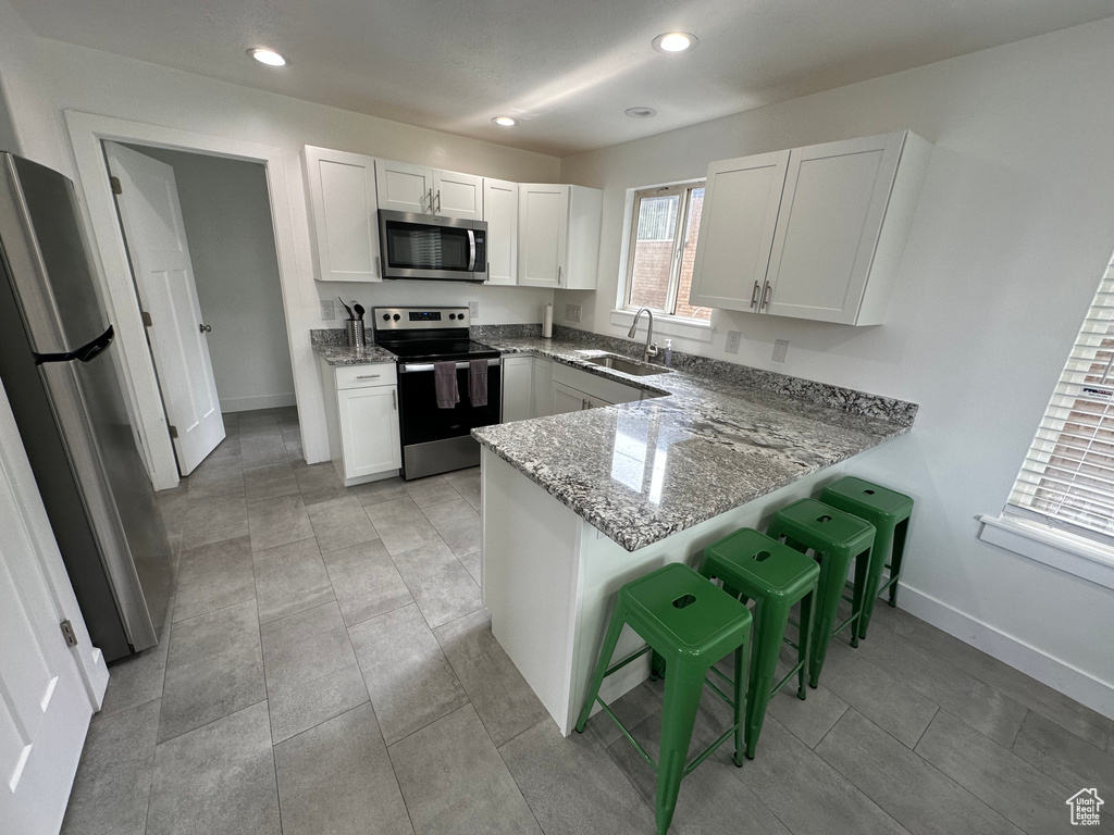 Kitchen with stainless steel appliances, a sink, a peninsula, light stone countertops, and baseboards