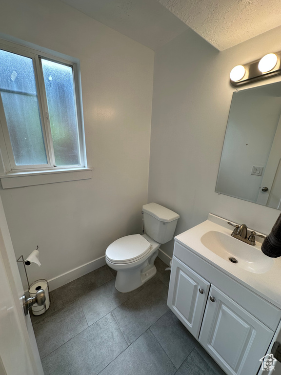 Bathroom with toilet, vanity, tile patterned floors, baseboards, and a textured ceiling