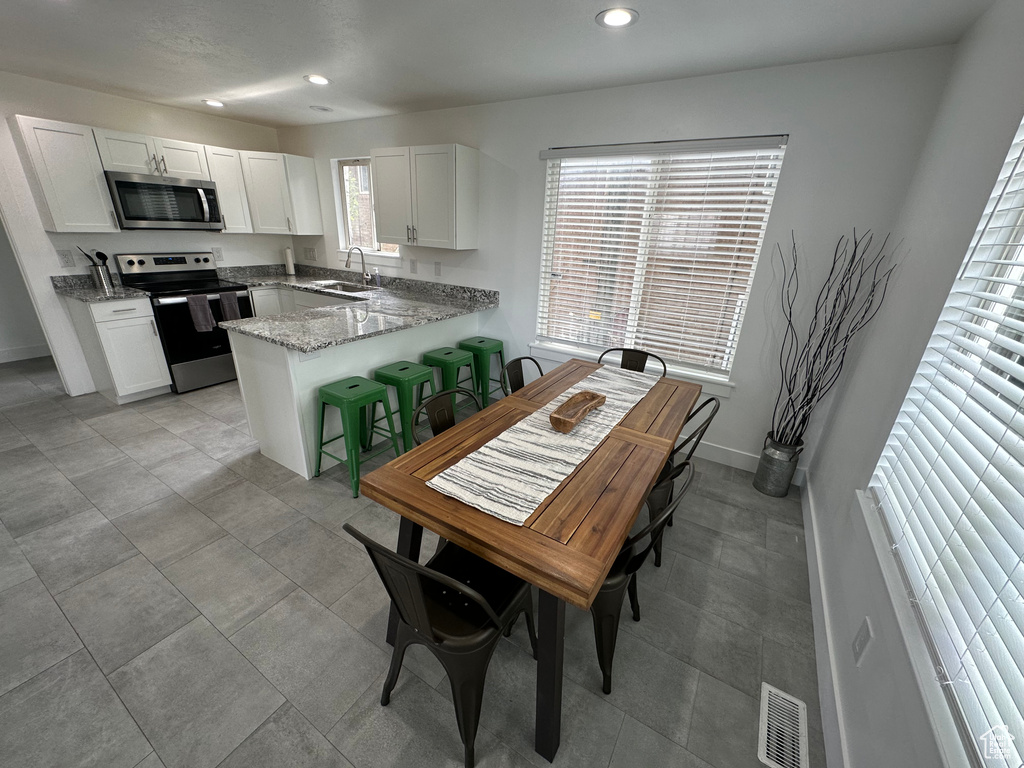 Kitchen with stainless steel appliances, a sink, recessed lighting, a peninsula, and white cabinetry