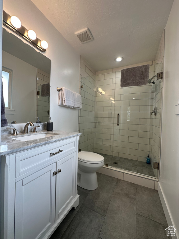 Full bath with tile patterned flooring, a stall shower, toilet, vanity, and a textured ceiling
