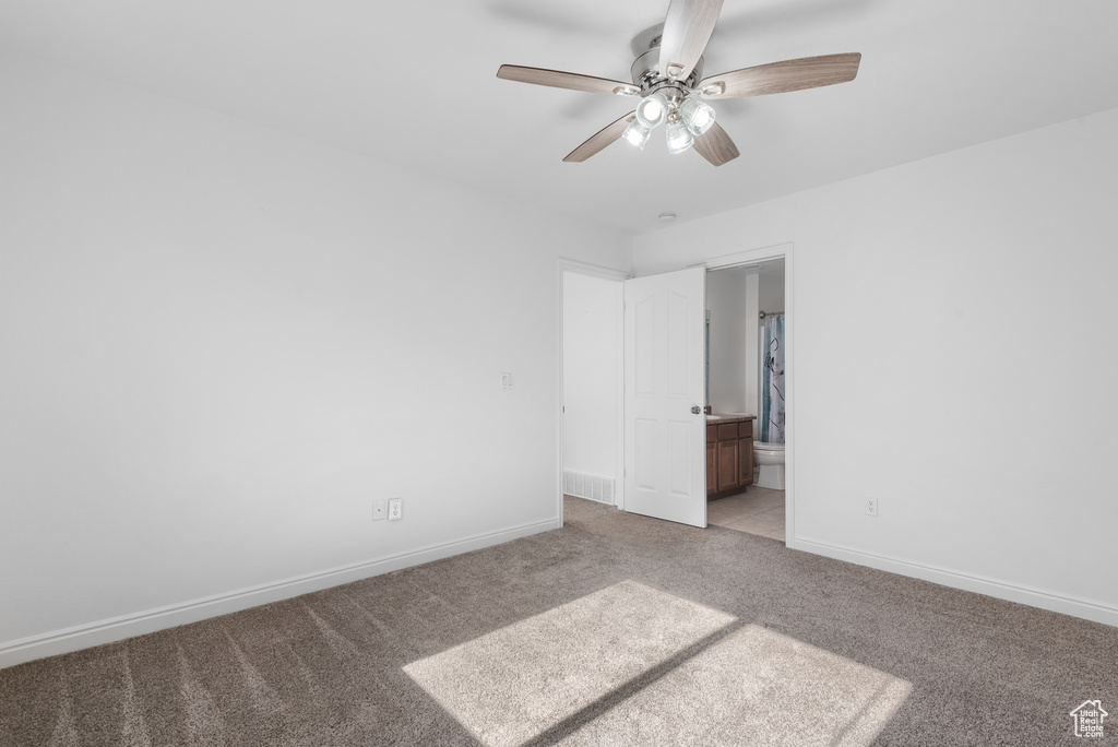 Unfurnished bedroom featuring light colored carpet, baseboards, ensuite bath, and ceiling fan