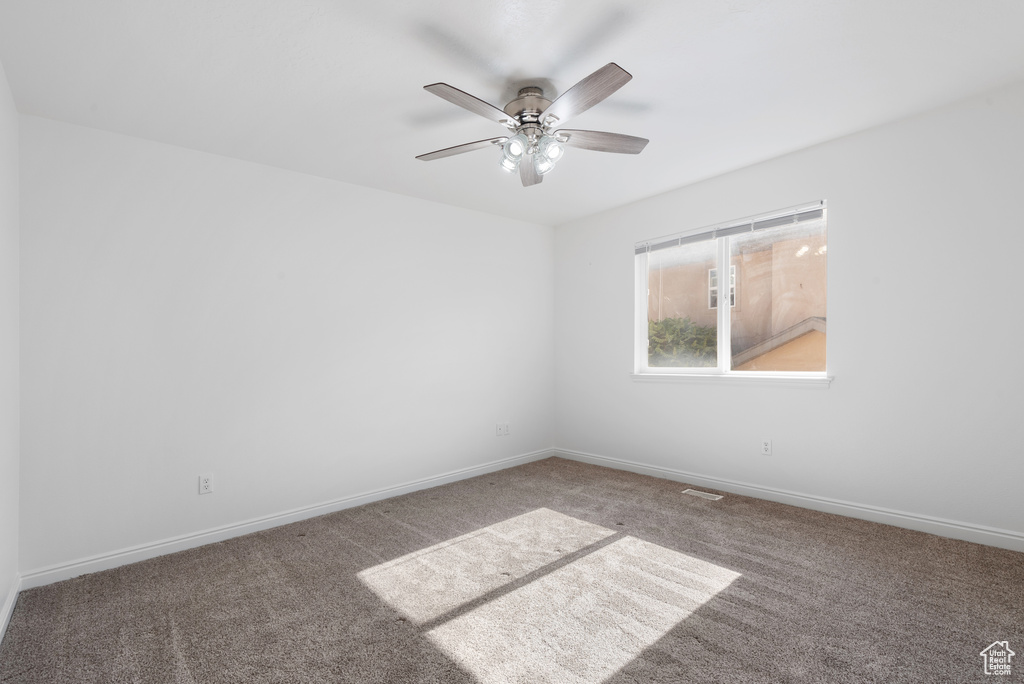 Carpeted spare room featuring ceiling fan and baseboards