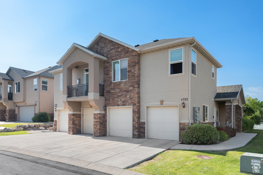 Multi unit property with stone siding, stucco siding, a garage, and concrete driveway