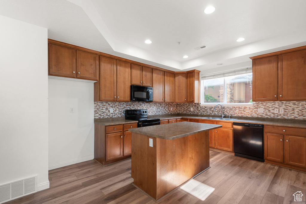 Kitchen featuring black appliances, a sink, dark countertops, brown cabinetry, and recessed lighting