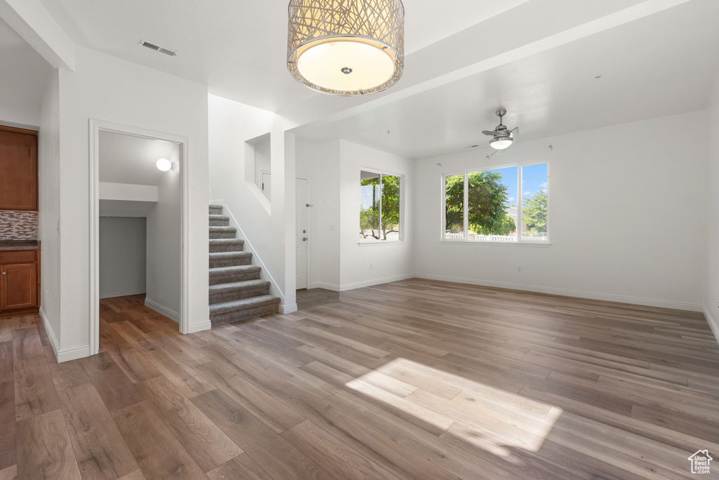 Unfurnished living room with stairway, light wood finished floors, ceiling fan, and baseboards