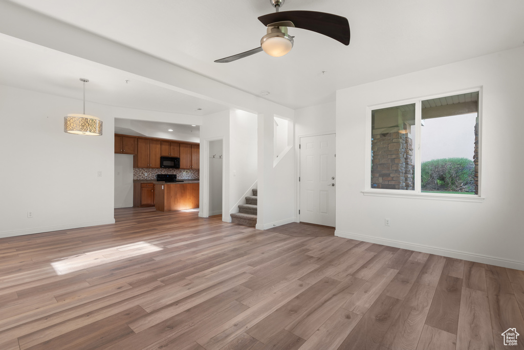 Unfurnished living room featuring stairway, ceiling fan, light wood-style floors, and baseboards